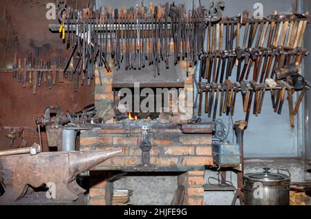 Le marteau du forgeron repose sur une enclume métallique à l'intérieur d'un ancien atelier de forgeron en flou. Banque D'Images