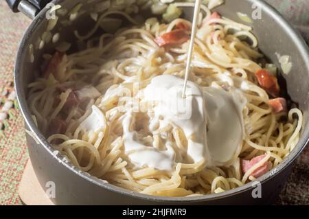 nouilles dans une casserole avec saucisse de calabresa et crème aigre, nouilles carbonara en préparation. Banque D'Images