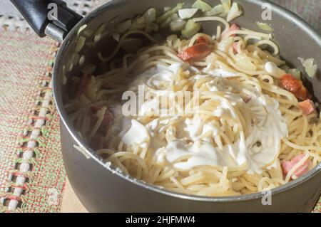 nouilles dans une casserole avec saucisse de calabresa et crème aigre, nouilles carbonara en préparation. Banque D'Images