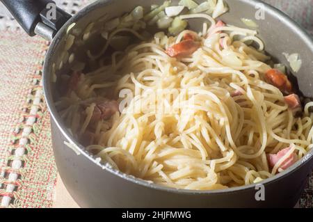 nouilles dans une casserole avec saucisse de calabresa et crème aigre, nouilles carbonara en préparation. Banque D'Images