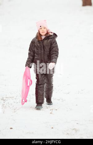 Bonne petite fille glissant sur la colline sur le traîneau de soucoupe.Fille appréciant le glisseur sur la neige Banque D'Images