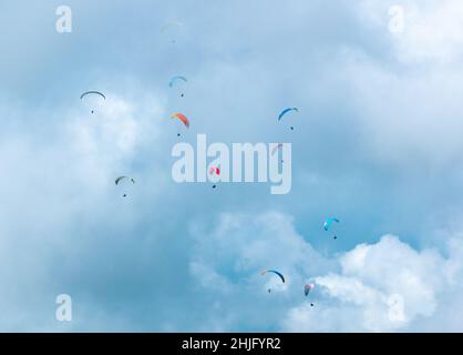 De nombreux Paragliders de différentes couleurs volant sur un fond bleu plein de nuages Banque D'Images