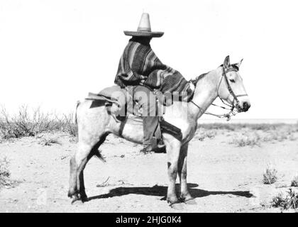 La photographie montre un homme à cheval en terrain désertique, portant un serape et un grand chapeau, identifié comme un scout indien pendant la Révolution mexicaine. Banque D'Images
