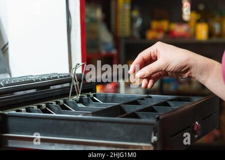 la main de la femme de latina prenant l'argent de la caisse, faisant une vente dans son magasin d'alimentation, fille prenant avec sa main une pièce colombienne de mille peso. Banque D'Images