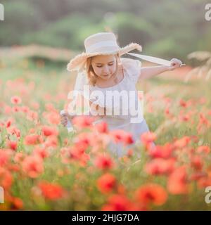 Une petite fille dans un chapeau marche à travers un champ de pavot.Heure d'été Banque D'Images