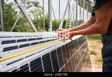 Gros plan des mains d'homme mesurant panneaux solaires photovoltaïques avec mètre ruban.Homme prenant des mesures avant d'installer des modules solaires pour produire de l'électricité par l'effet photovoltaïque. Banque D'Images