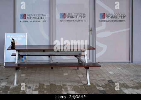 Devant la vitre d'un centre d'essais rapides Corona - tests citoyens - se trouve une table en bois et deux bancs.Sur la table se trouvent deux bouteilles de bière vides. Banque D'Images