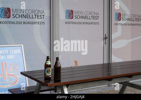 Devant la vitre d'un centre d'essais rapides Corona - tests citoyens - se trouve une table en bois et deux bancs.Sur la table se trouvent deux bouteilles de bière vides. Banque D'Images