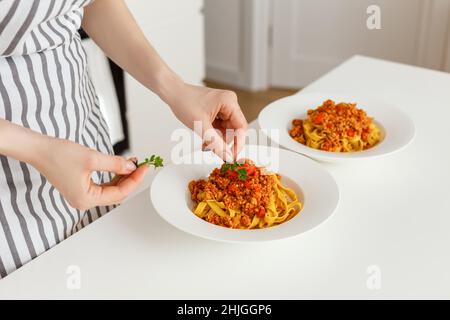 Femme gros plan les mains décorant les pâtes bolognaises avec la feuille de persil sur le dessus.Préparation de repas italien traditionnel à partir de nouilles.Plat avec des aliments sains faits maison. Banque D'Images