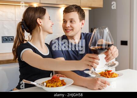 Dîner romantique à la maison le jour de la Saint-Valentin.Joyeux couple souriant, se régler des verres et manger des pâtes avec du vin à la cuisine.Concept de style de vie domestique, d'amour, de mariage heureux et de la convivialité. Banque D'Images