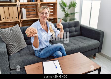 Belle femme travaillant au bureau de consultation souriant heureux et positif, pouce vers le haut faisant excellent et signe d'approbation Banque D'Images