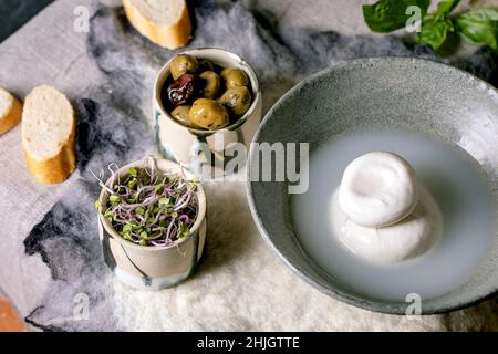 Fromage traditionnel italien burrata noué dans un bol en céramique grise sur la table.Pain, olives, salade verte.Ingrédients pour DIN méditerranéen sain Banque D'Images