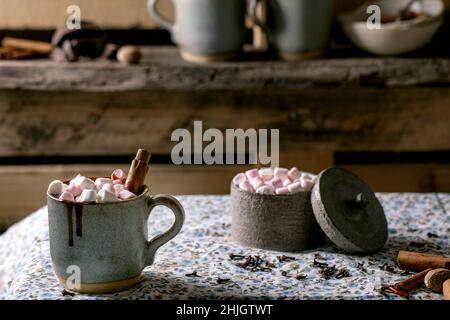 Une tasse de boisson d'hiver au chocolat chaud et épicé avec guimauve, bâton de cannelle, épices et un pot de guimauve sur une nappe en lin rustique.Pays k Banque D'Images