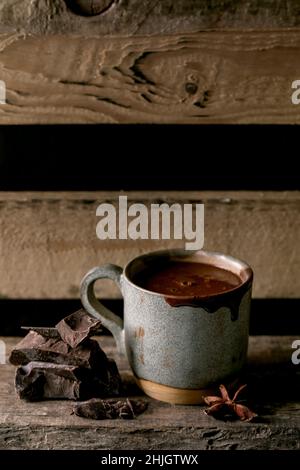 Une tasse de chocolat chaud épicé, une boisson d'hiver maison avec une barre de chocolat noir hachée sur une ancienne étagère en bois.Boisson chaude et confortable. Banque D'Images