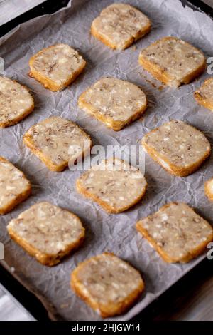 Couper de la pâte sablée maison pour cuire des biscuits au sucre avec des noix et du chocolat blanc sur la plaque de cuisson avec du papier de cuisson sur le linge blanc cuisine à Banque D'Images