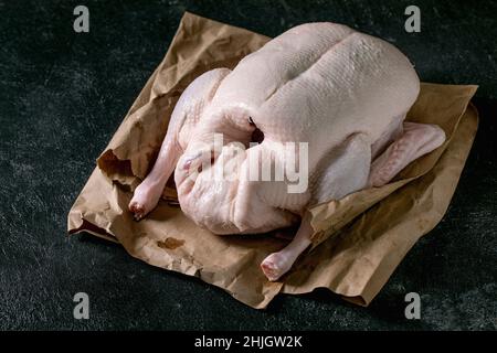 Jeune canard entier non cuit biologique cru sur papier froissé sur fond de texture noire.Gros plan Banque D'Images