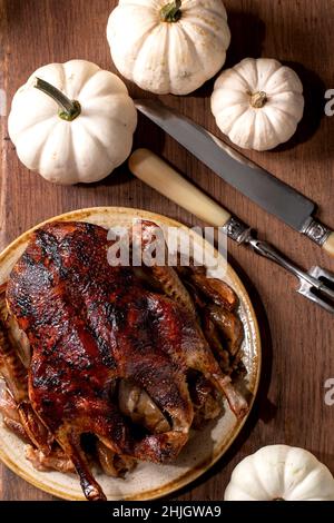 Table de vacances avec plats classiques canard glacé rôti avec pommes en plaque de céramique sur table en bois avec décoration d'automne citrouilles blanches.Pose à plat Banque D'Images