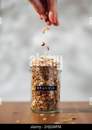 Une femme verse à la main du granola maison sans gluten dans un bol en verre Banque D'Images