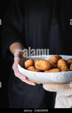 Croquettes de pommes de terre détenues par une femme sur un dessus noir, avec espace de copie Banque D'Images