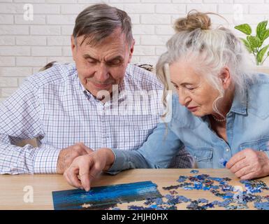 Un couple senior dans leur 80s , à la recherche des pièces du puzzle qu'ils assemblent à la maison Banque D'Images