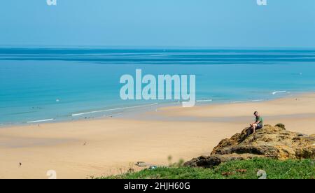 Newquay,Cornouailles,Angleterre,Royaume-Uni-juin 21st 2021: Un homme utilise son téléphone tout en étant assis sur un rocher dans le chaud mi-été soleil.surplombant le wi Banque D'Images