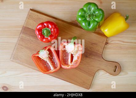 Vue de dessus du poivron rouge coupé sur la planche à découper avec poivrons tricolores dispersés Banque D'Images