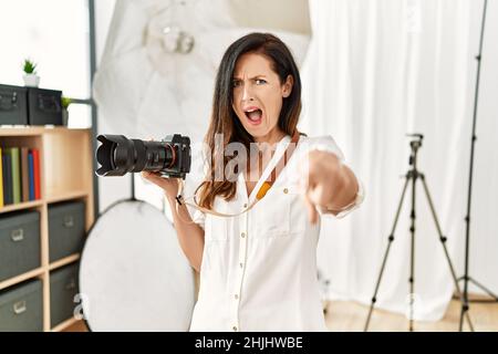 Belle femme caucasienne travaillant en tant que photographe au studio de photographie montrant mécontente et frustrée de l'appareil photo, furieux et furieux avec vous Banque D'Images