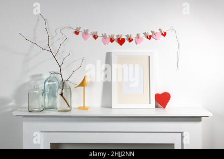 Décoration pour la Saint-Valentin.Une guirlande de coeurs en feutre sur une cheminée décorative.Cadre photo, un vase avec une branche, un cadeau dans une boîte en forme de coeur, Banque D'Images