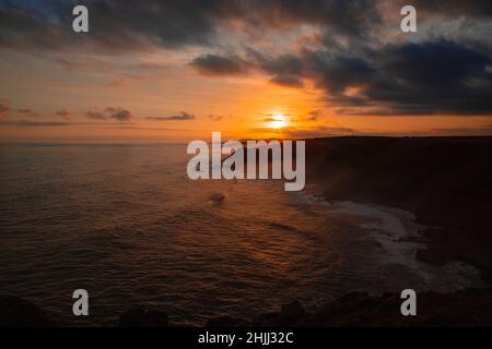 Morgan Bay Cliffs sur la côte sauvage à un coucher de soleil sombre brumeux Banque D'Images