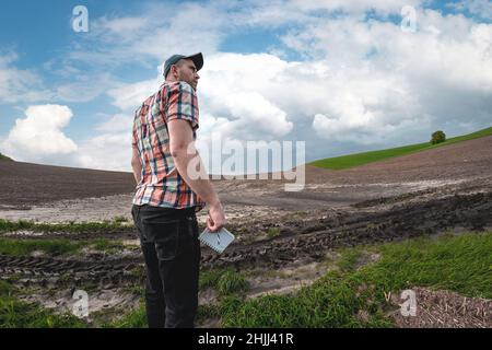 Un agronome mâle examine les champs après de fortes pluies sur fond de nuages pluvieux.Évaluation des dommages météorologiques terres agricoles après les inondations Banque D'Images