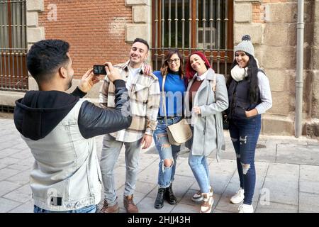 Latino homme prenant une photo avec son smartphone de son groupe d'amis dans une rue de ville. Banque D'Images