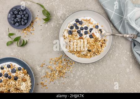 vue de dessus d'une grande assiette de granola et yaourt, bleuets mûrs et noix. le concept d'une alimentation saine et équilibrée. fond en béton gris Banque D'Images