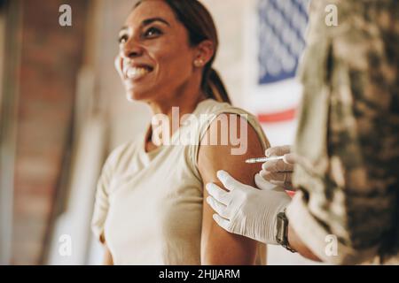 Femme soldat recevant une dose du vaccin Covid-19 dans son bras.La servicewoman des États-Unis souriant joyeusement tout en se faisant inoculer contre corona Banque D'Images