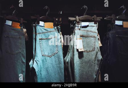 Dans un magasin de vêtements, des jeans tendance de différentes couleurs, tailles et modèles sont accrochés à des cintres.Shopping et vente.Choisir des vêtements à acheter. Banque D'Images