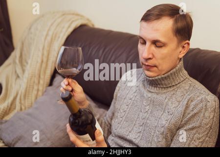 Décontracté, serein, riche, solitaire, d'âge moyen, un homme seul boit du vin rouge, se détendant sur un canapé à la maison, se reposant sur un canapé tenant une dégustation de verre Banque D'Images