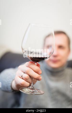 Décontracté, serein, riche, solitaire, d'âge moyen, un homme seul boit du vin rouge, se détendant sur un canapé à la maison, se reposant sur un canapé tenant une dégustation de verre Banque D'Images