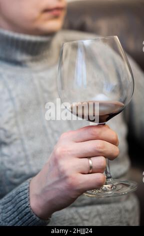 Décontracté, serein, riche, solitaire, d'âge moyen, un homme seul boit du vin rouge, se détendant sur un canapé à la maison, se reposant sur un canapé tenant une dégustation de verre Banque D'Images