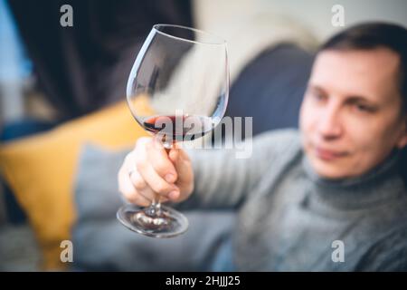 Décontracté, serein, riche, solitaire, d'âge moyen, un homme seul boit du vin rouge, se détendant sur un canapé à la maison, se reposant sur un canapé tenant une dégustation de verre Banque D'Images