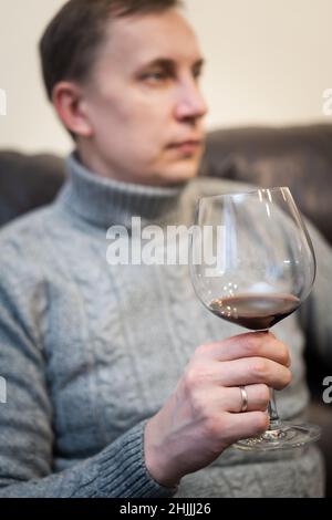 Décontracté, serein, riche, solitaire, d'âge moyen, un homme seul boit du vin rouge, se détendant sur un canapé à la maison, se reposant sur un canapé tenant une dégustation de verre Banque D'Images