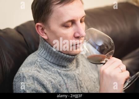 Décontracté, serein, riche, solitaire, d'âge moyen, un homme seul boit du vin rouge, se détendant sur un canapé à la maison, se reposant sur un canapé tenant une dégustation de verre Banque D'Images