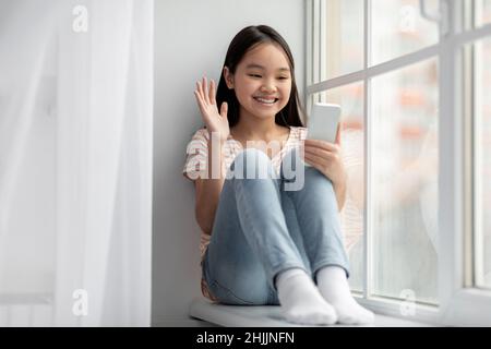 Gamin asiatique joyeux ayant la vidéo conférence avec ses amis Banque D'Images