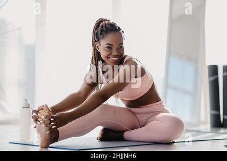 Bonne sportive jeune femme noire en vêtements de sport étirant son corps à la maison, sur toute la longueur Banque D'Images