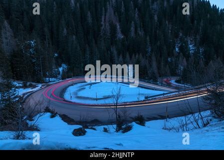 Sentiers légers sur une route sinueuse dans les Alpes européennes au crépuscule en hiver Banque D'Images