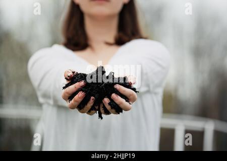 Jeune femme devant un jardin avec ses mains tendues tenant du compost frais pour le jour de la Terre.Focalisation extrême sélective sur les doigts et le sol. Banque D'Images
