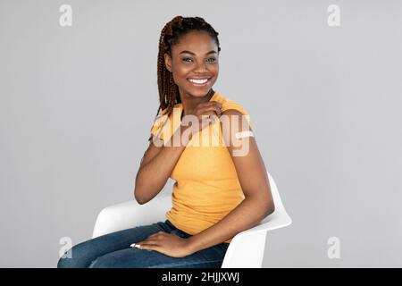 Femme afro-américaine souriant après avoir reçu le vaccin contre le coronavirus sur fond gris studio Banque D'Images