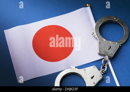Drapeau et menottes sur fond bleu, un concept sur le thème de la criminalité dans la société japonaise, vue de dessus Banque D'Images