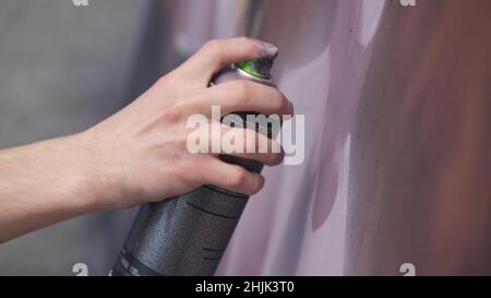 Une main avec un vaporisateur qui dessine un nouveau graffiti sur le mur. Photo de l'élaboration d'un graffiti sur un mur en bois close-up. Le concept de st Banque D'Images