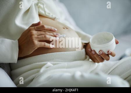 Gros plan de la femme enceinte appliquant de la crème de soin de la peau sur son ventre pour empêcher la marque d'étirement Banque D'Images