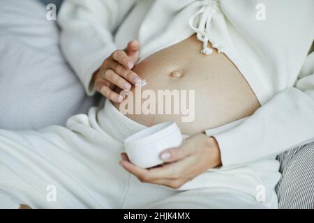 Gros plan d'une jeune femme enceinte appliquant une crème anti-stretch sur son ventre pendant la grossesse Banque D'Images