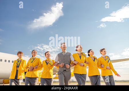 Homme et femme souriants, les agents de bord portant un uniforme d'aviation lorsqu'ils marchent près de l'avion à l'aéroport Banque D'Images